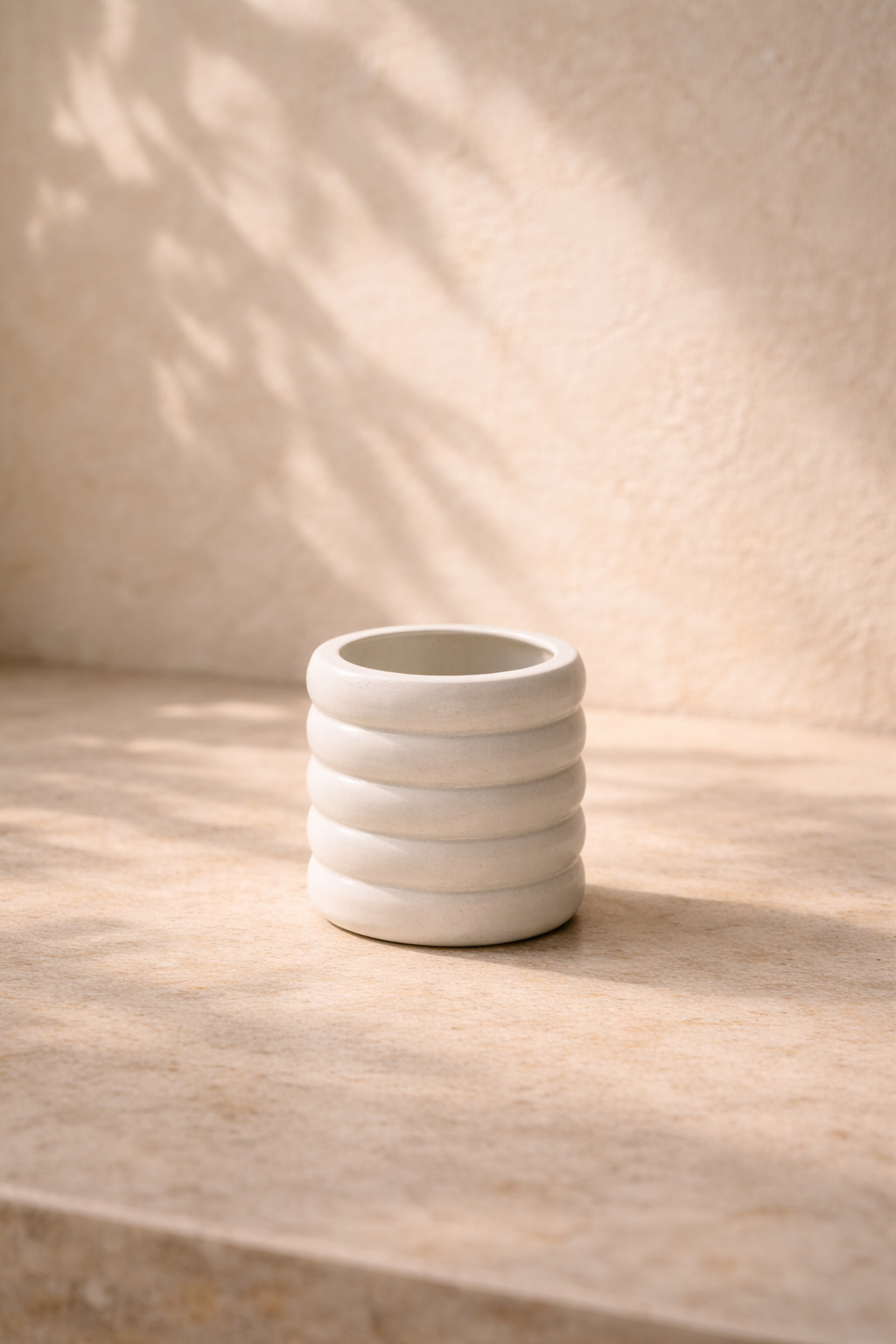 Matte white ribbed cylindrical candle vessel with horizontal grooves in mineral composite on neutral background.