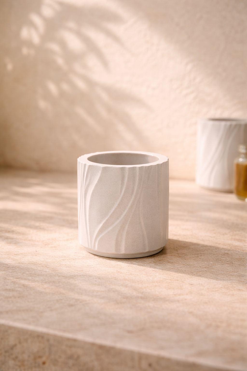 Lit candle in matte white cylindrical vessel with vertical tree-like texture in mineral composite on neutral background.